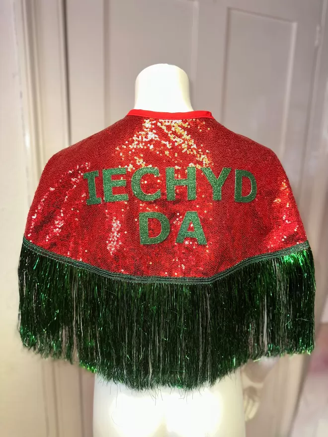 a midi cape with red sequins, green text reading 'IECHYD DA' and green tinsel