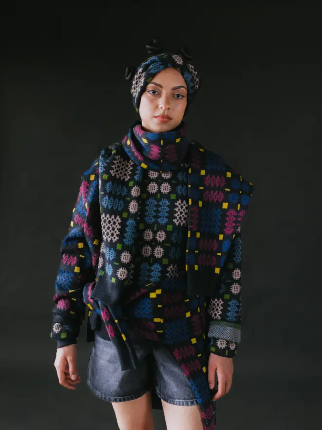 Model wearing pieces from MABLI's 'Carthen' collection, featuring the Carthen Wrap in the vibrant 'Fireworks' colour-way. The design showcases bold, colourful patterns inspired by traditional Welsh blanket tapestry.