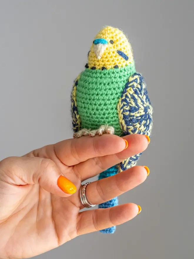 Budgerigar Hand Crocheted Figure, a green crocheted bird sitting on a wooden poll. 