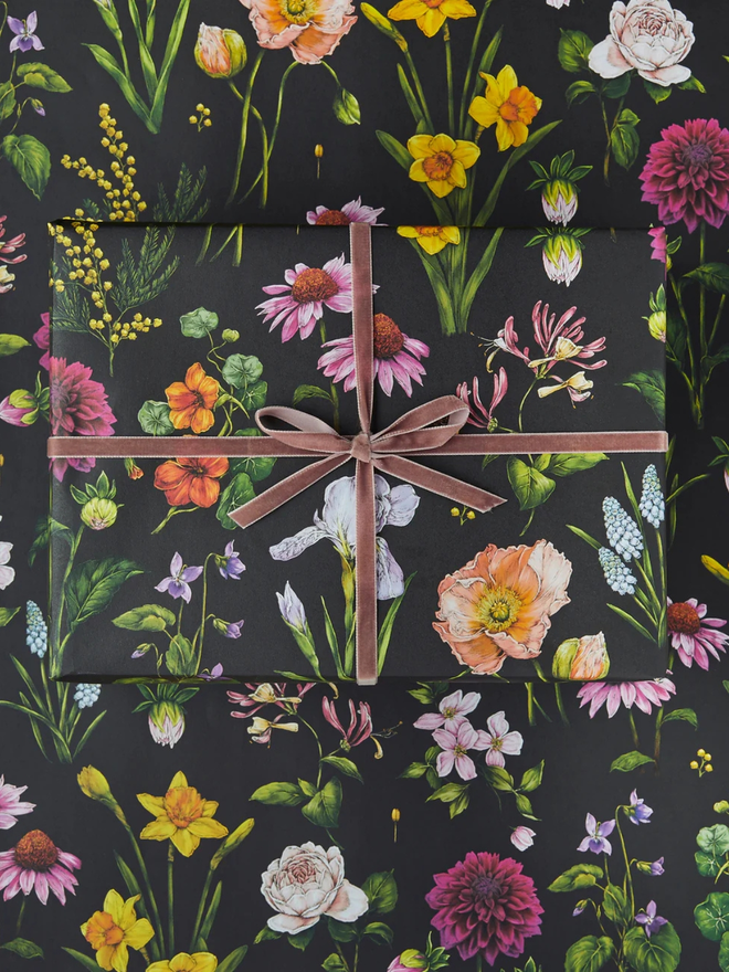 bountiful blooms floral gift wrap sheet. a box wrapped in black illustrated floral gift wrap with a purple ribbon.