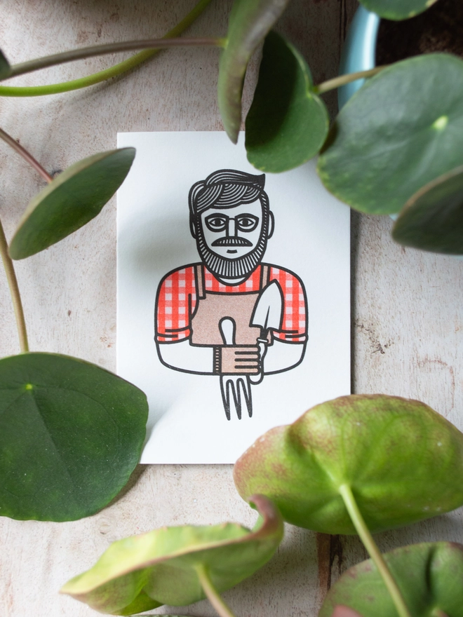 A card for gardeners with a bold and modern illustration of a character in a red gingham shirt with the sleeves rolled up holding gardening tools is surrounded by green leaves and plants.