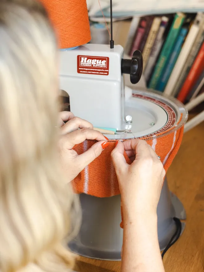 Orange wristwarmers being attached by two hands to a linking machine with edges being linked together.