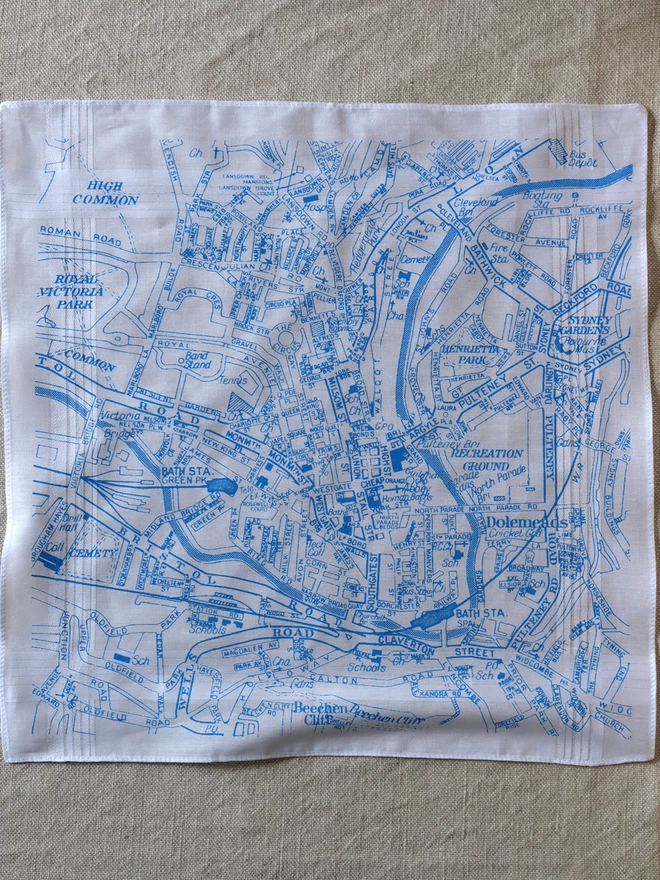 A Mr.PS Bath map hankie printed in sky blue laid flat on a linen cloth