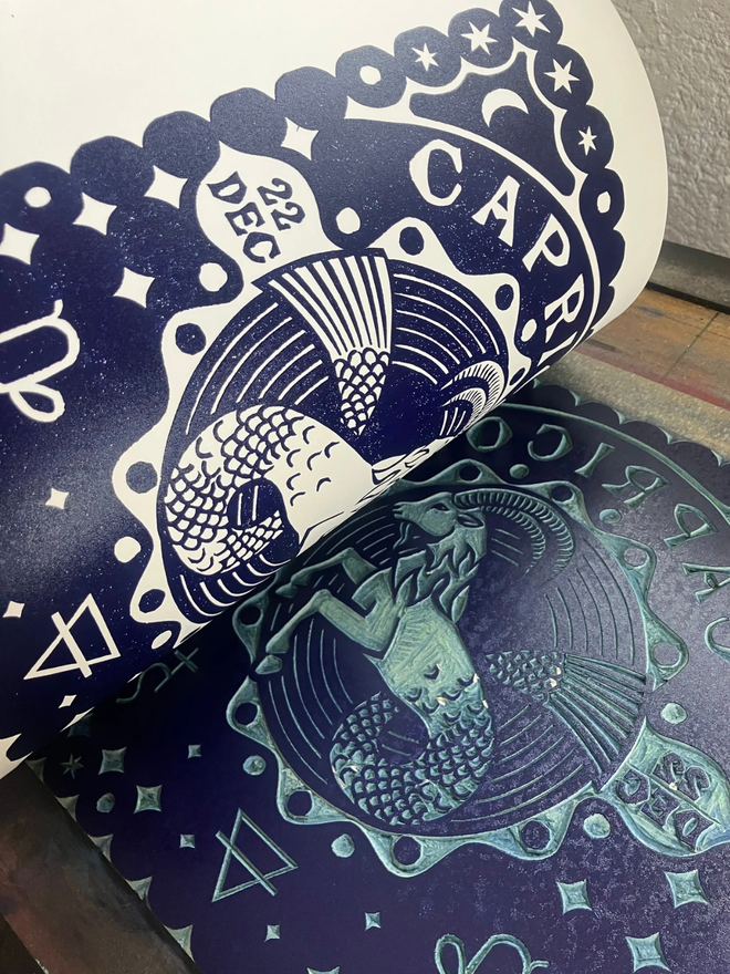 capricorn zodiac linocut. a linocut goat and zodiac symbols printed on a blue background.