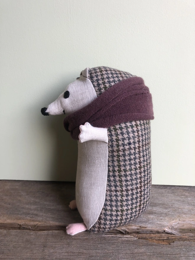 Handmade fabric toy hedgehog made from natural linen (front) and brown tweed (back) wearing a burgundy woollen scarf. Side view.