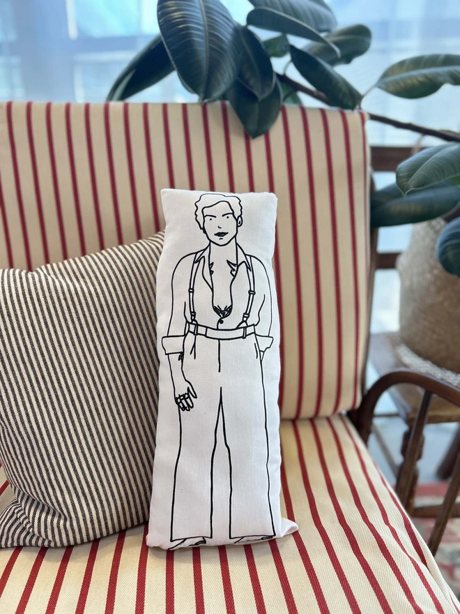 Black and white screen printed cushion featuring an illustration of Harry Styles, on a sofa with striped cushions.