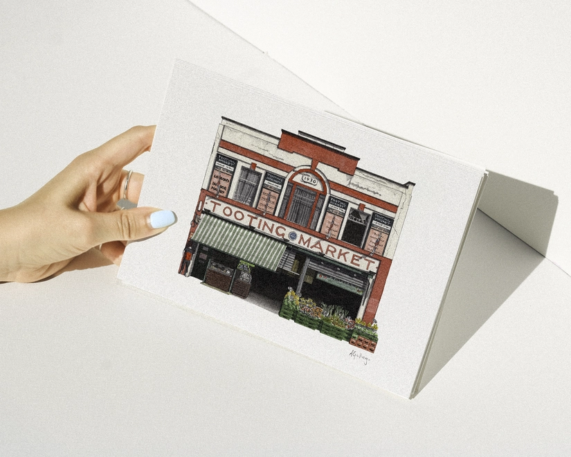 A hand with blue nail polish holding a print featuring an illustration of the Tooting Market entrance with its red and white facade and green-striped awning against a white background.