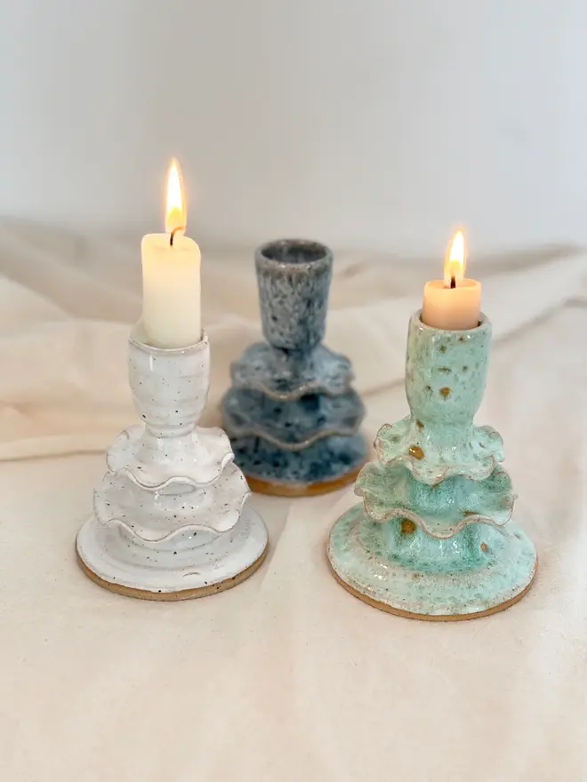 three ceramic candlestick holders in white, blue, and green, two of which are holding lit candles