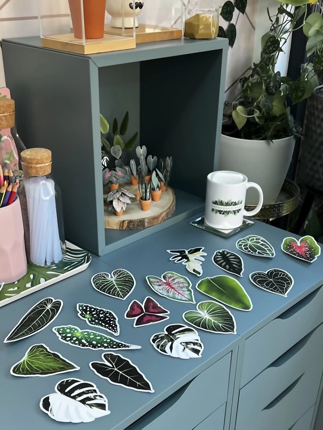 A selection of plant stickers laid out on a blue desk with ornaments and plants in the background.