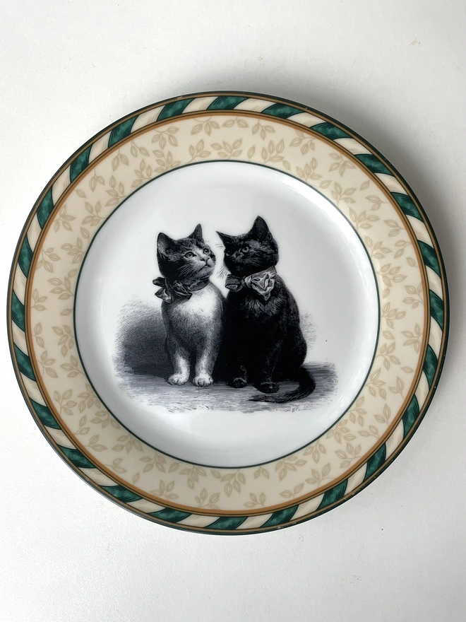 a vintage plate with a pea green border with gold trim and in the centre is an illustration of a pair of Victorian kittens