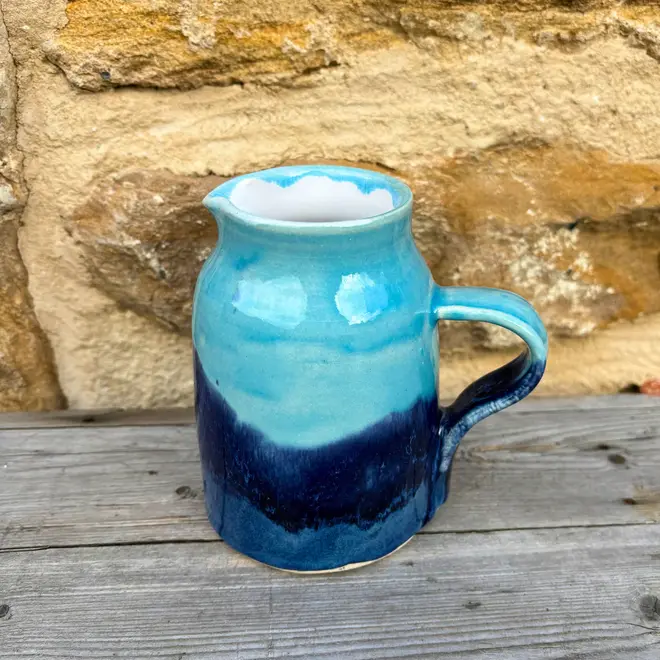Landscape Medium Jug, a colourful jug sitting on a wooden surface against a brick backdrop. 