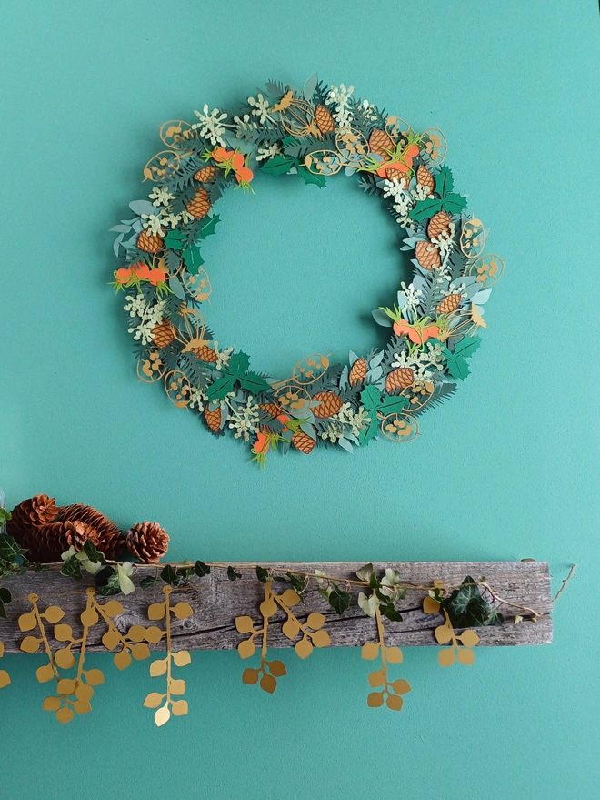 winter foliage papercut wreath displayed on wall above mantelpiece decorated with papercut garland