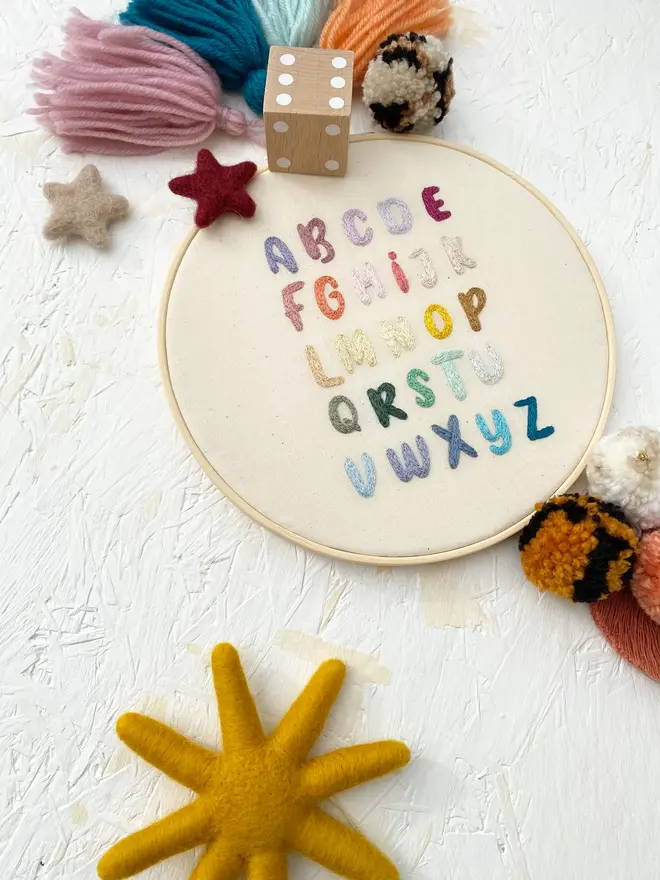 letters of the alphabet embroidered hoop. colourful stitch alphabet hoop on plain white background.