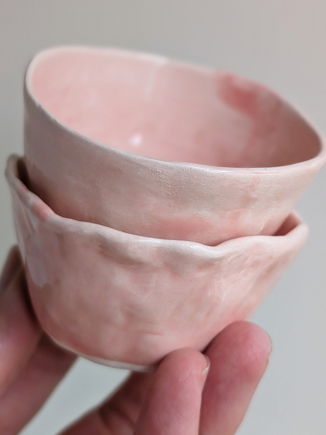 two pink ceramic pinch pots held aloft in a hand