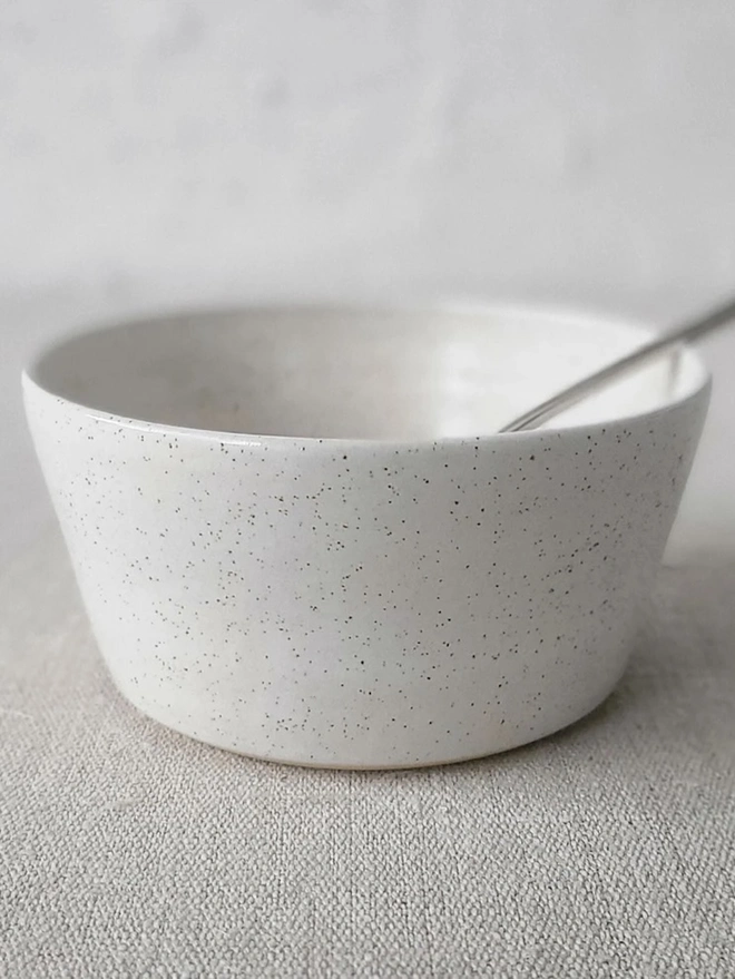 Classic Ceramic Breakfast Bowl, a breakfast bowl sitting on a grey carpet against a plain backdrop. It is accompanied by some cereal and a spoon. 