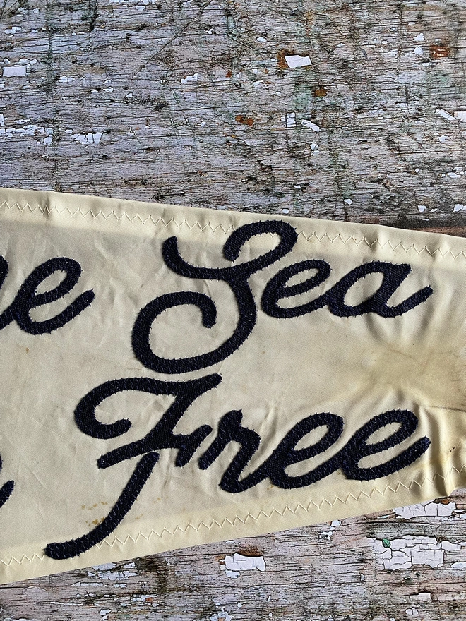 Detail of an up cycled sail cloth 'Keep the sea plastic free' pennant flag showing the words sea and free in navy canvas