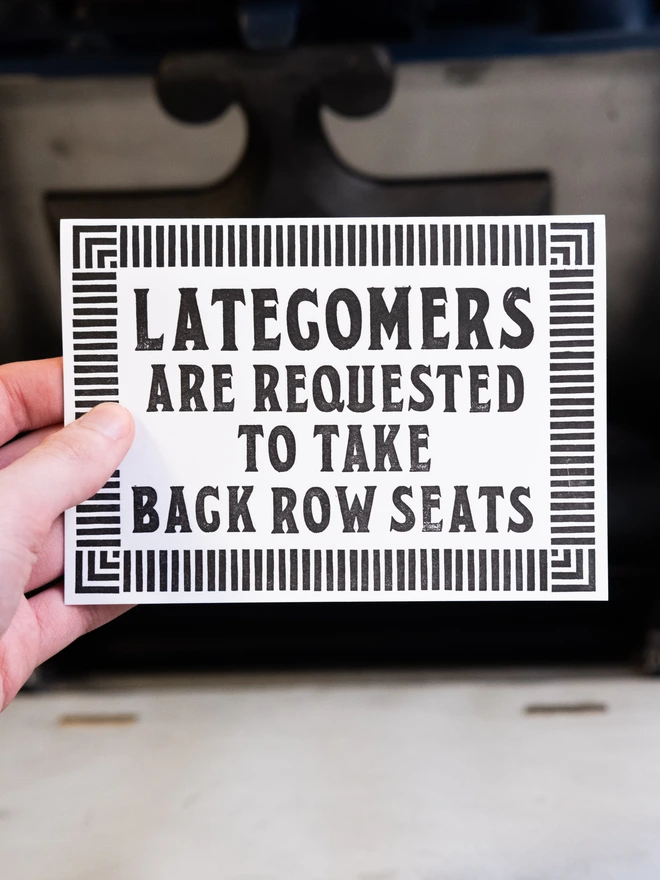 Letterpress card with text design "Latecomers are requested to take back row seats," Surrounded by art deco style border of parallel lines. 