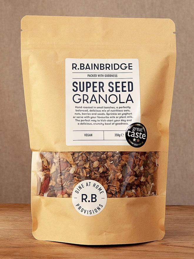 Super Seed Granola Packet, a pack of granola sitting on a wooden surface in front of a plain backdrop. 