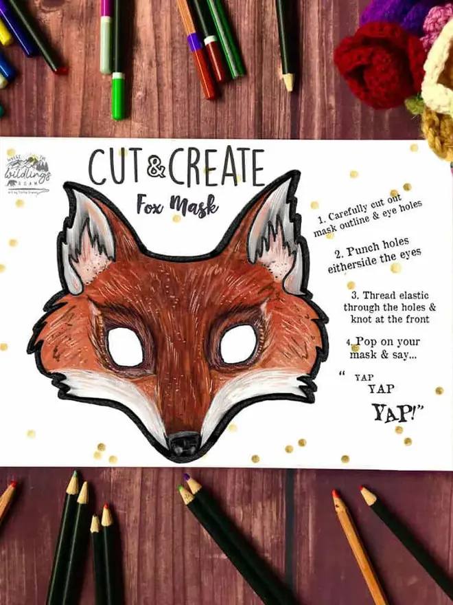 Cut And Create Forest Animals Children’s Masks Kit, an illustrated fox face, surrounded by coloured pencils on a dark wood background.