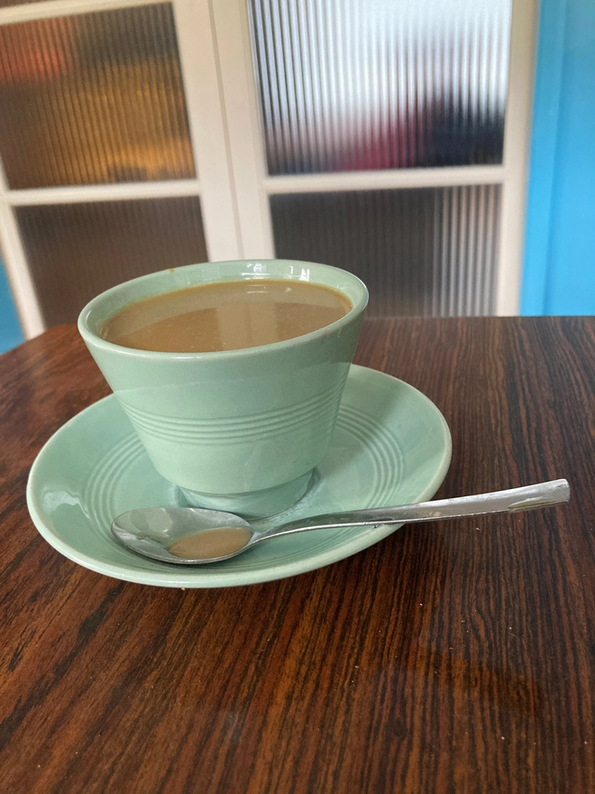 A pale green 1940s cup and saucer from the company Beryl Ware. The cup is filled to the brim with resin ‘tea’. There is a tea spoon in the saucer which has a drop of resin tea in its bowl.