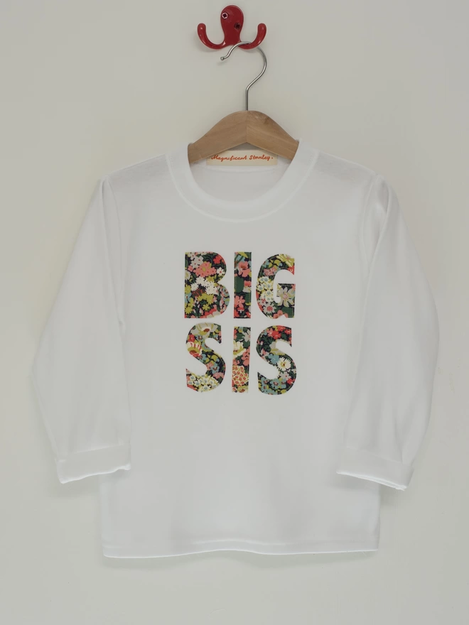big sis appliquéd on a long sleeve white cotton t-shirt hanging on a hanger