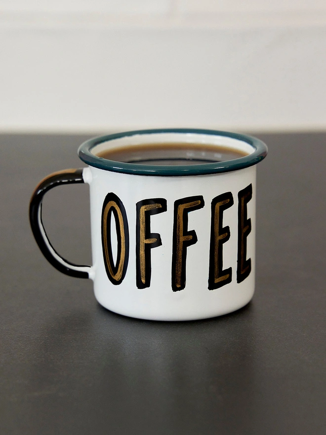 White enamel mug with 'coffee' sign written on the front in blue and gold