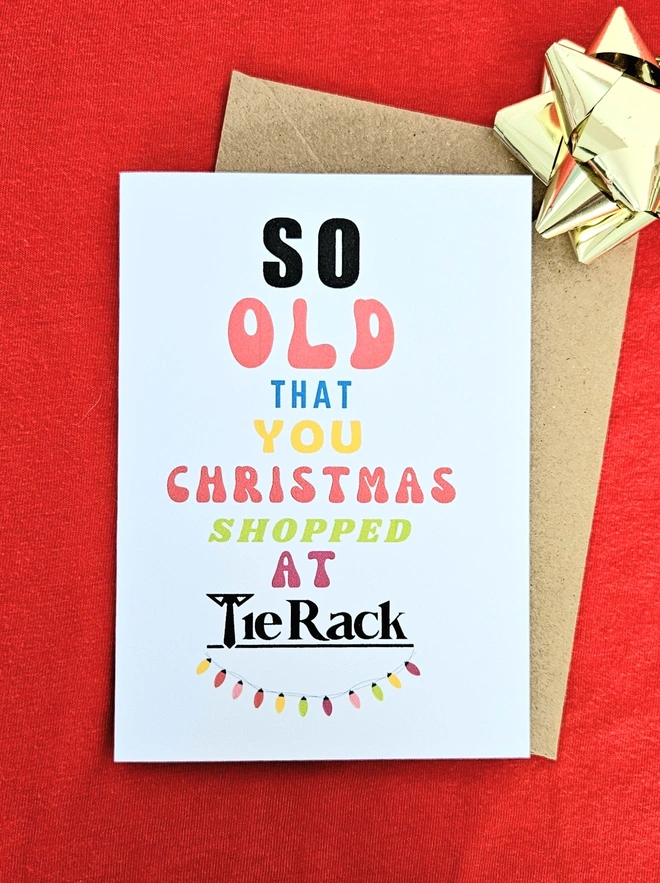 A photograph of the front of a humorous A6 greeting card illustrated using brightly coloured text and the retro shop logo. The text says so old you Christmas shopped at Tie Rack with illustrated string fairy lights.