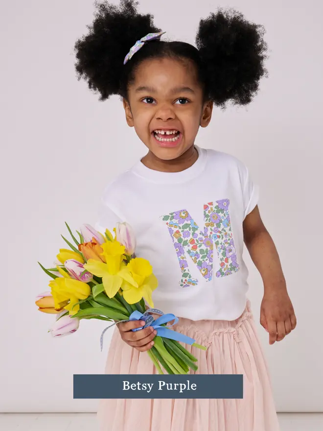 a 3 year old girl wearing a personalised kids white t-shirt with an initial cut from liberty floral print on the front