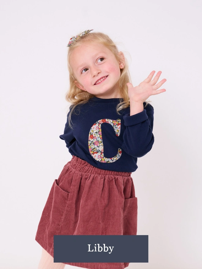 a 4 year old girl wearing a personalised navy kids cotton t-shirt with her initial on in Liberty floral fabric