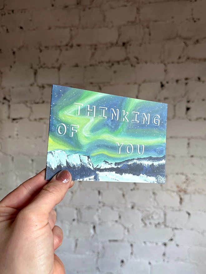 a greetings card featuring an illustration of the northern lights landscape with the text “thinking of you”