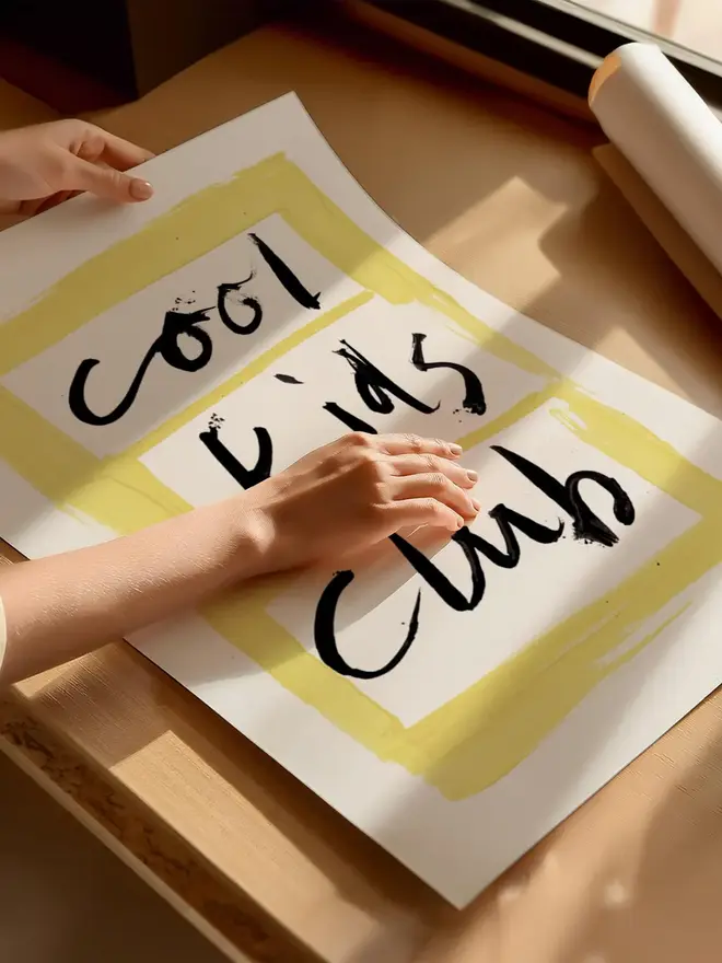 'cool kids club' art print. a print with a white and yellow background with a slogan in black lettering being rolled up.
