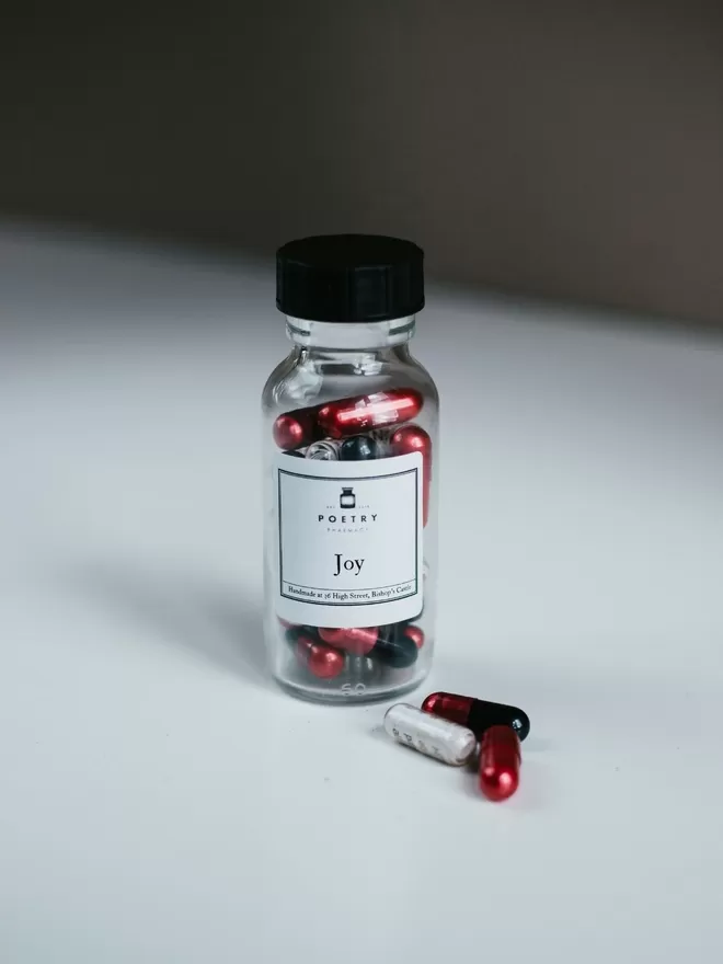 Glass bottle with Joy poems in pills seen on a white table