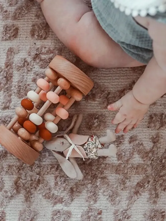 rolling wooden abacus rattle toy. a wooden rattle toy with silicone and wooden abacus beads on a nursery floor.
