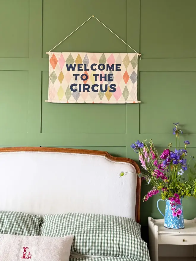 'Welcome To The Circus' Cotton Wall Hanging, hanging on a green wall. 