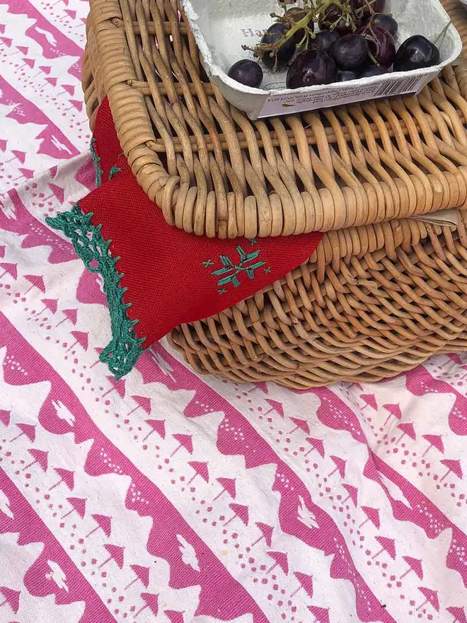 Pink Belle Mare Woven Throw, a pink throw accompanied by a wooden hamper with a bowl of fruit on top of it. 