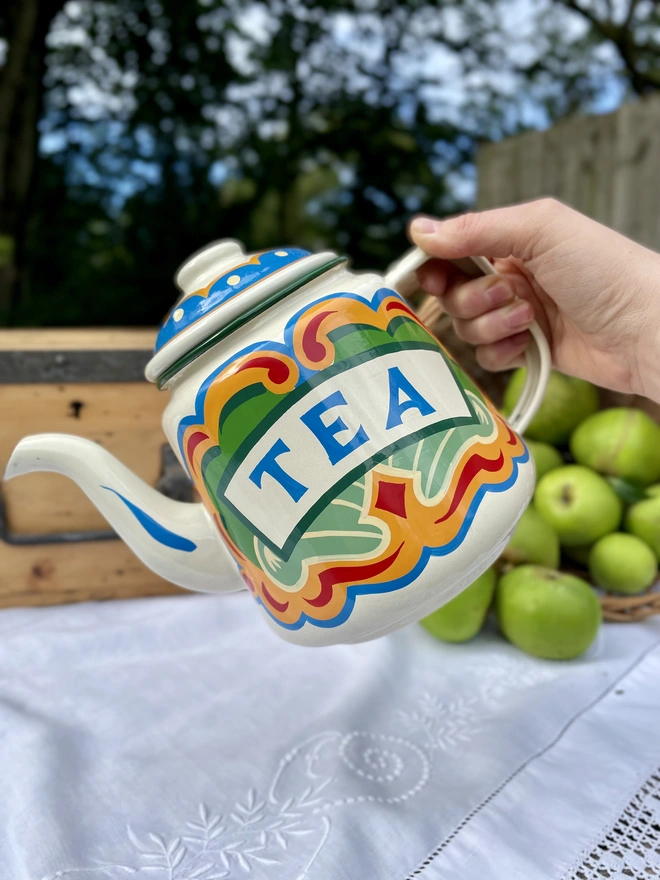Cream vintage teapot, hand painted with a fairground design in green, blue, yellow and red. ‘Tea’ is painted in a banner across the centre.