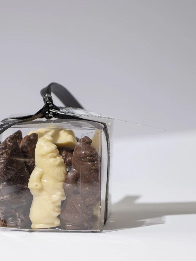 A clear cube filled with Milk, White and Dark chocolate Santa and Reindeer figures, tied with ribbon and a tag