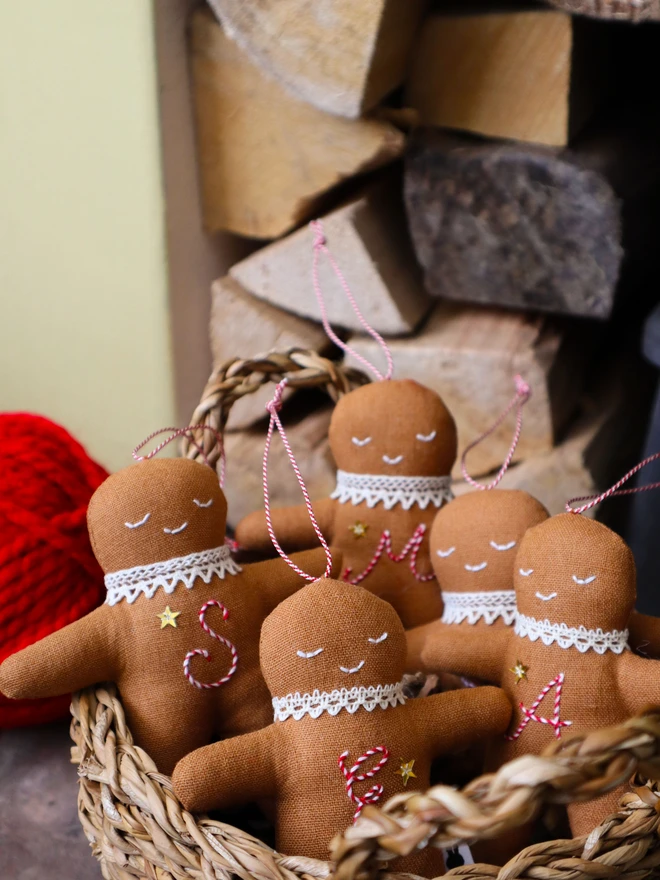 Brown linen gingerbread man christmas tree ornament with a letter hand embroidered in candy cane colours, star shaped sequin, crochet cotton lace around the neck, smile embroidered in white and candy cane colour string to hang. 