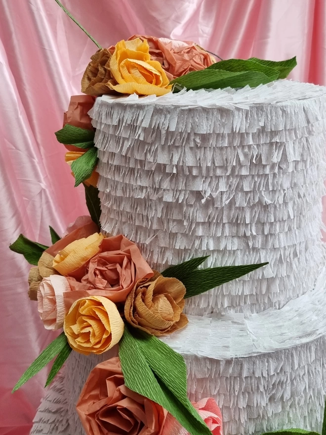 close up of blush crepe paper flowers on wedding cake pinata in front of a ponk satin backdrop