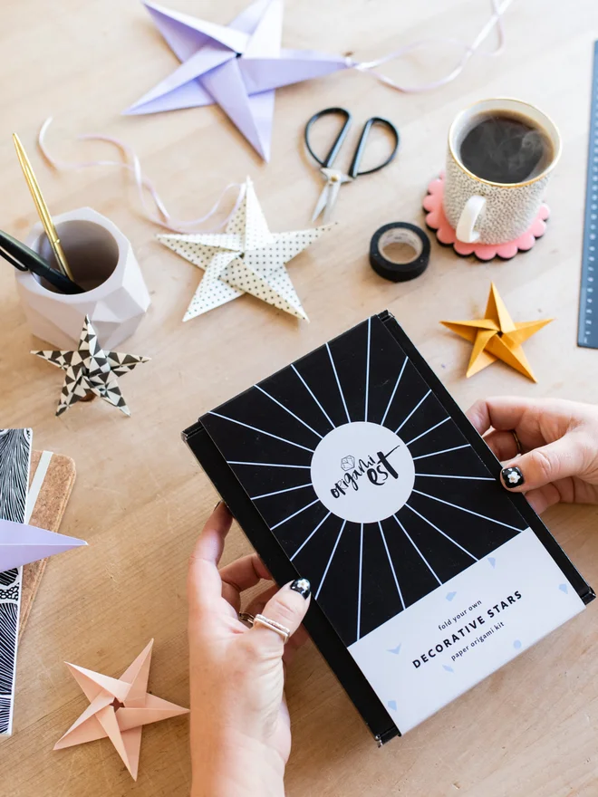 Woman holding origami kit with origami stars scattered on table
