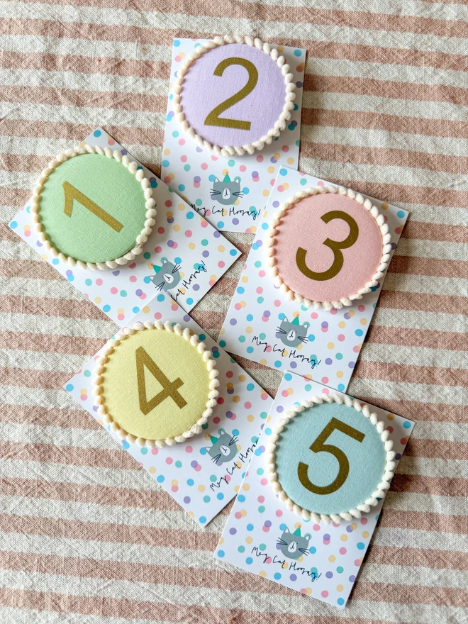 pink, blue, green, yellow and lilac birthday number badges with a pompom trim 
