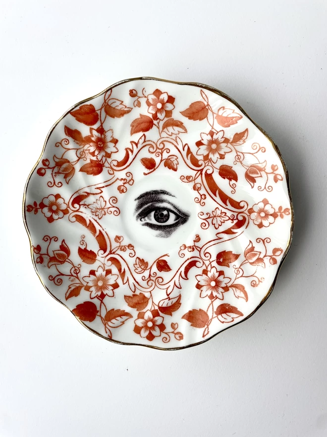vintage plate with an ornate border, with a printed vintage illustration of a eye in the middle 