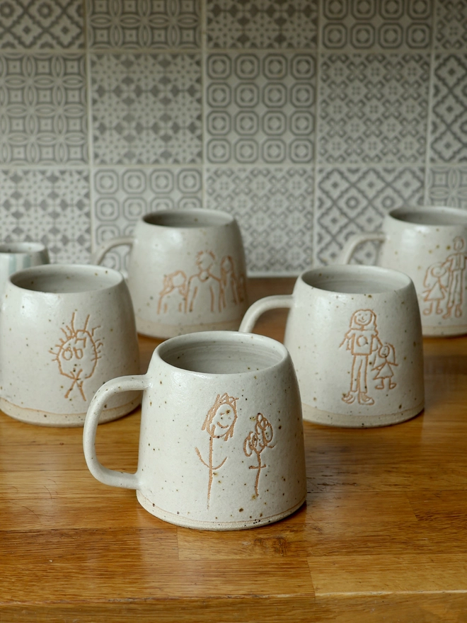 5 Childrens Drawing Handmade Ceramic Mugs on a wooden kitchen counter. 