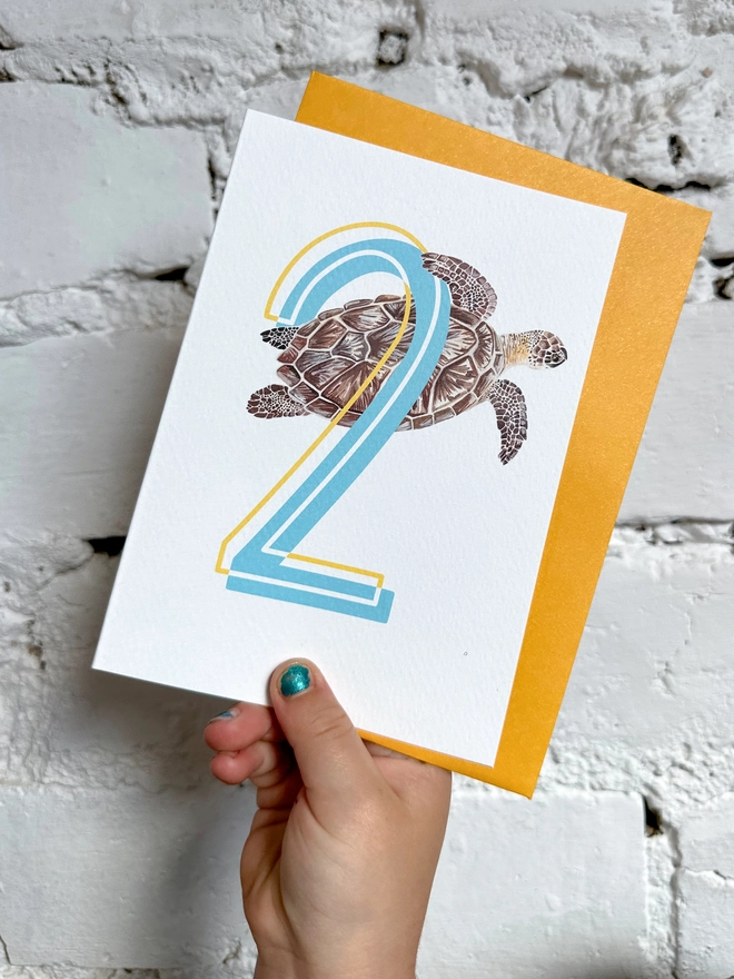 a white card with a big blue number 2 and a turtle illustration with a bright yellow envelope