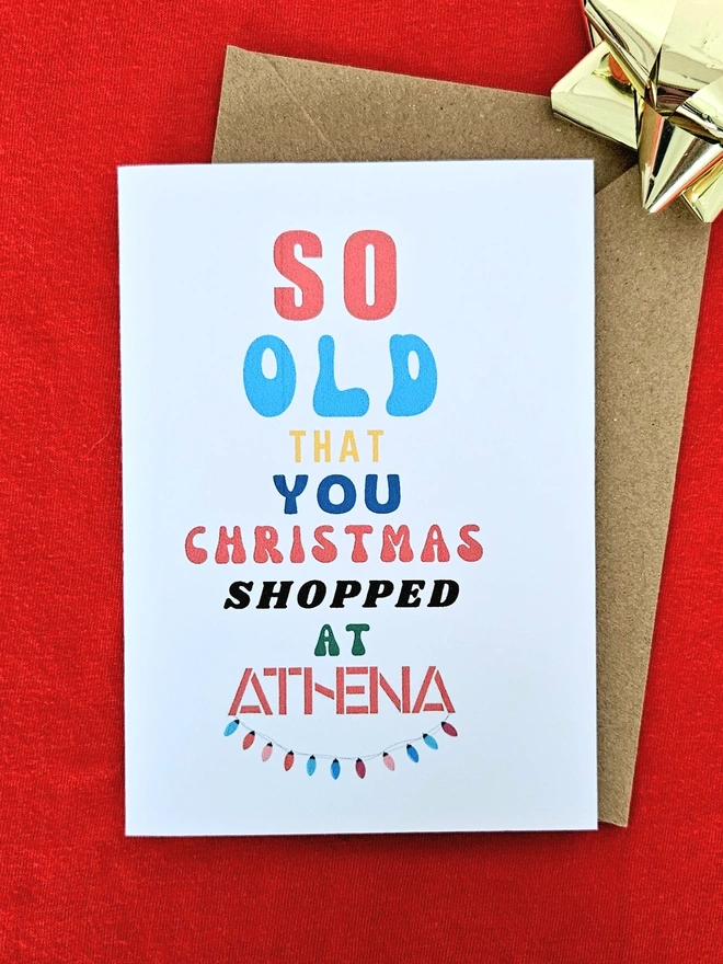 A Christmas Card that says so old you christmas shopped at Athena with a string of fairy lights on a white background woth a borwn envelope.