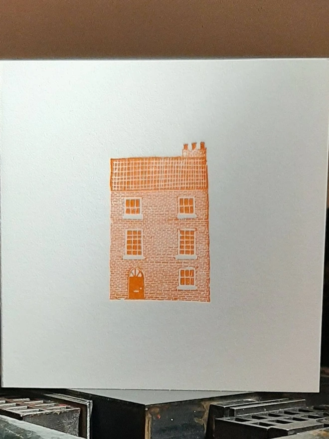 Orange Townhouse Letterpress Handprinted Greetings Card, a white card with an orange townhouse design in the centre. 