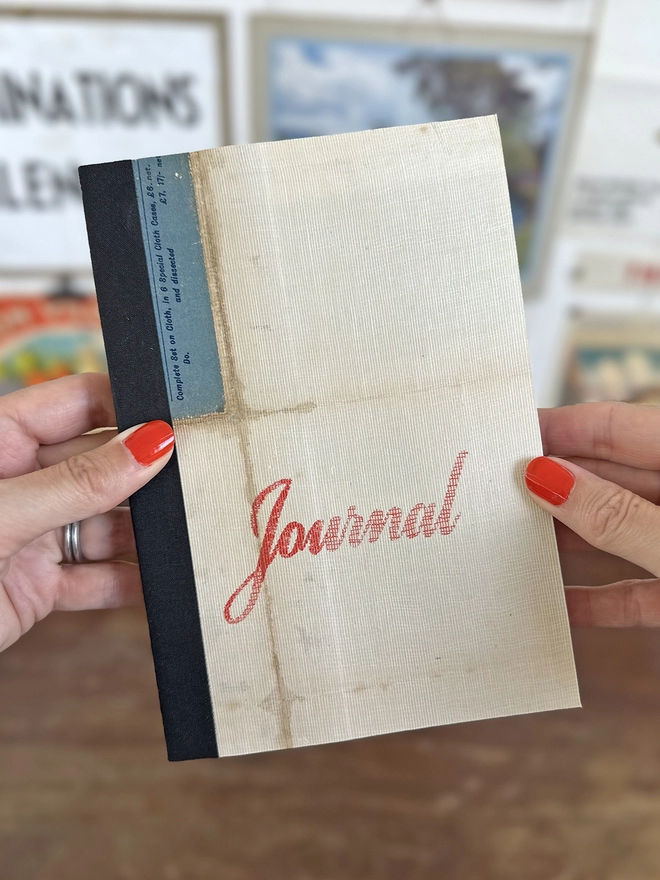 Holding the red script linen map journal with black cloth binding and red printed type
