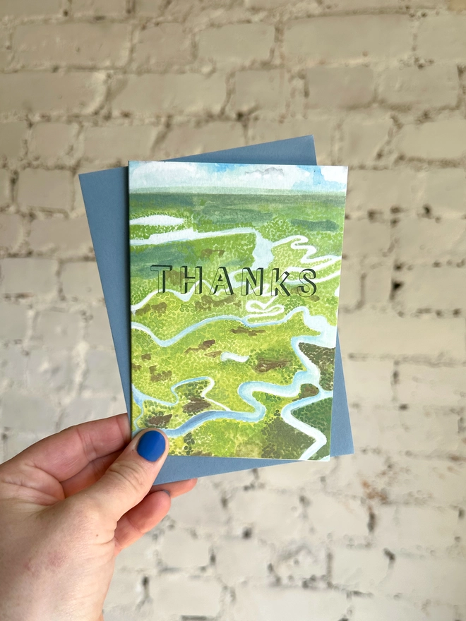 a greetings card featuring an illustration of the everglades landscape with the text “thanks” with a blue envelope