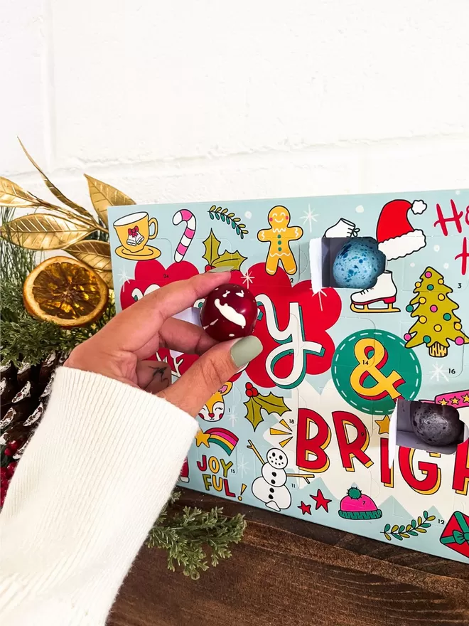 a hand holding a chocolate with a red and white  design - set above a fireplace next to a decorated christmas tree
