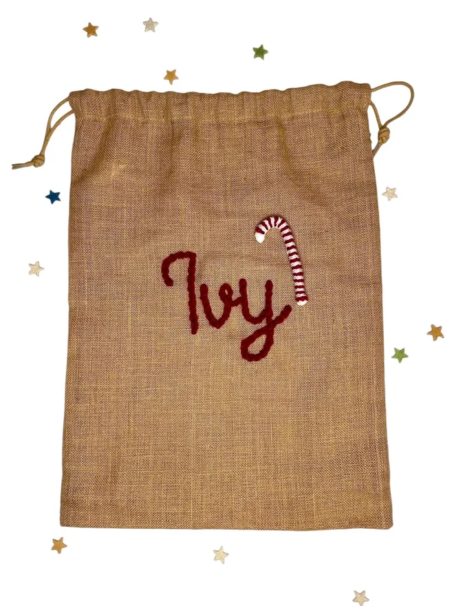 Personalised Christmas Sacks Ivy, a Christmas sack sitting on a white surface. It has its own personalisation, is surrounded by stars, and is accompanied by a candy cane design. 